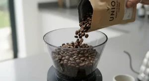 Freshly roasted coffee beans being poured into the hopper of the quietest coffee grinder, preparing for a perfect morning brew.