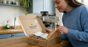 Alt text for image 3: Freshly roasted VALOR ROASTERS coffee being smelled and unpacked from a branded delivery box by a man in a British kitchen, highlighting quality and freshness.