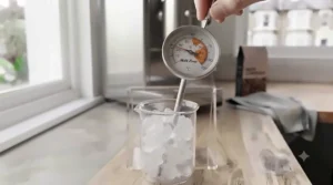 Testing the accuracy of an espresso milk thermometer in a glass of ice water during calibration.