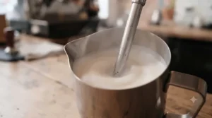 Professional steam wand texturing silky microfoam inside a stainless steel milk pitcher