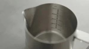 Clear internal measurement markings inside a stainless steel milk pitcher for accurate liquid volume.
