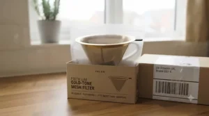 A brand new gold-tone coffee filter in its minimal retail packaging, ready for home delivery.